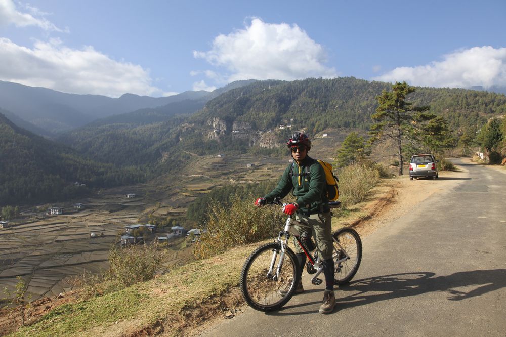 A cyclist pausing above terraced rice fields on a Bhutan valley road